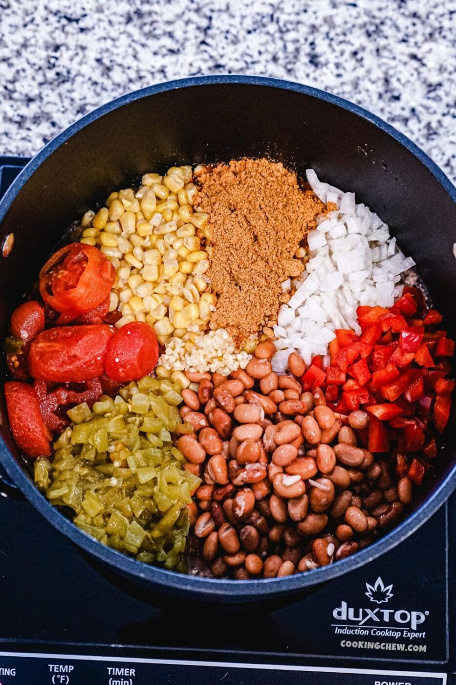 A stainless steel pot filled with colorful taco soup ingredients simmers on an induction cooktop. 