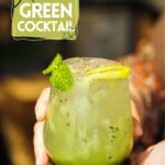 A person holding a glass of a kiwi mojito.