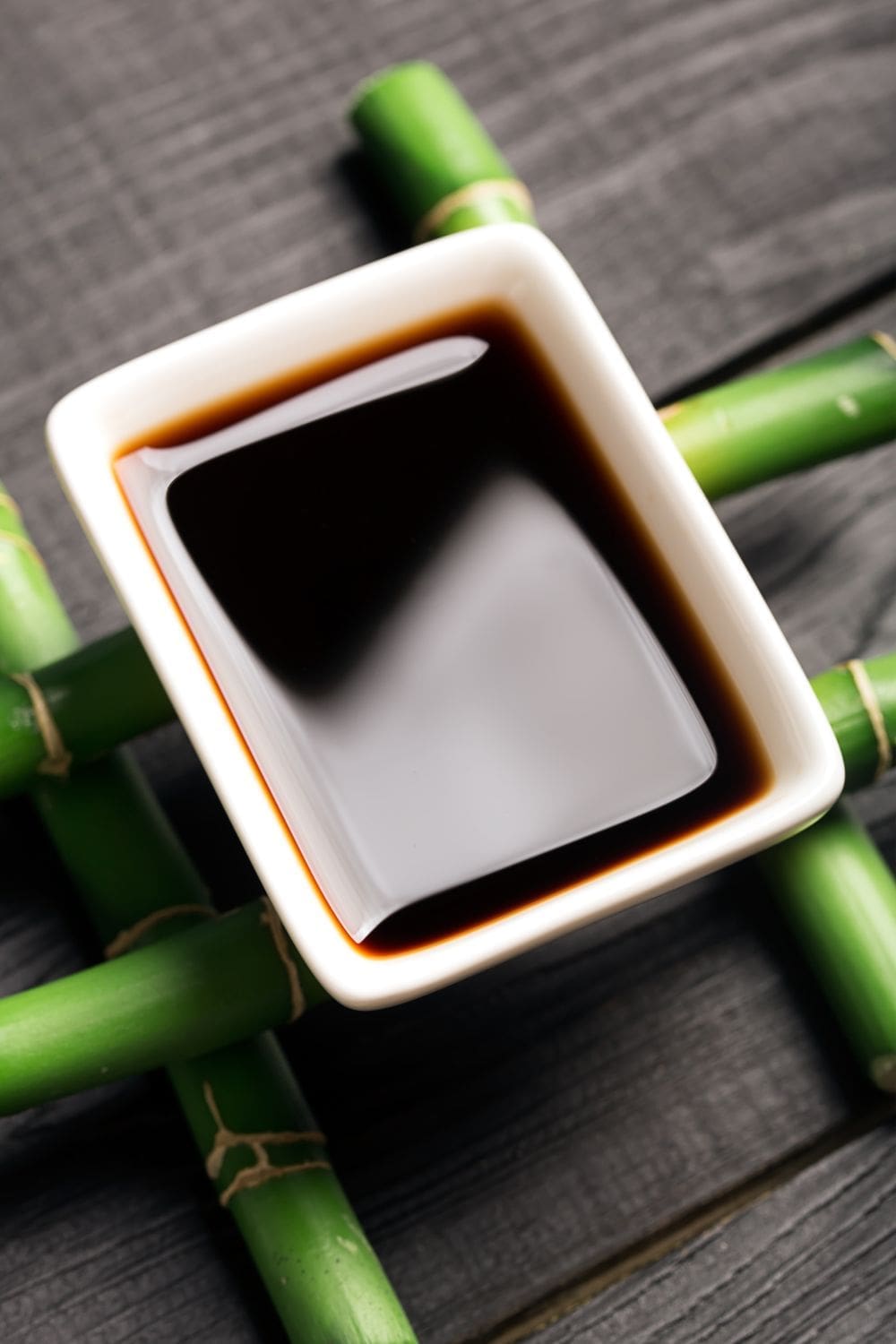 A square, ceramic bowl filled with tamari sauce sits on a bamboo frame.