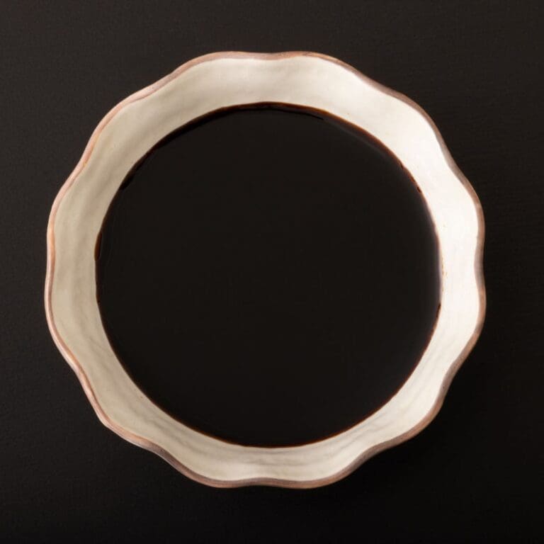 A close-up photo of a bowl of tamari on a black background.