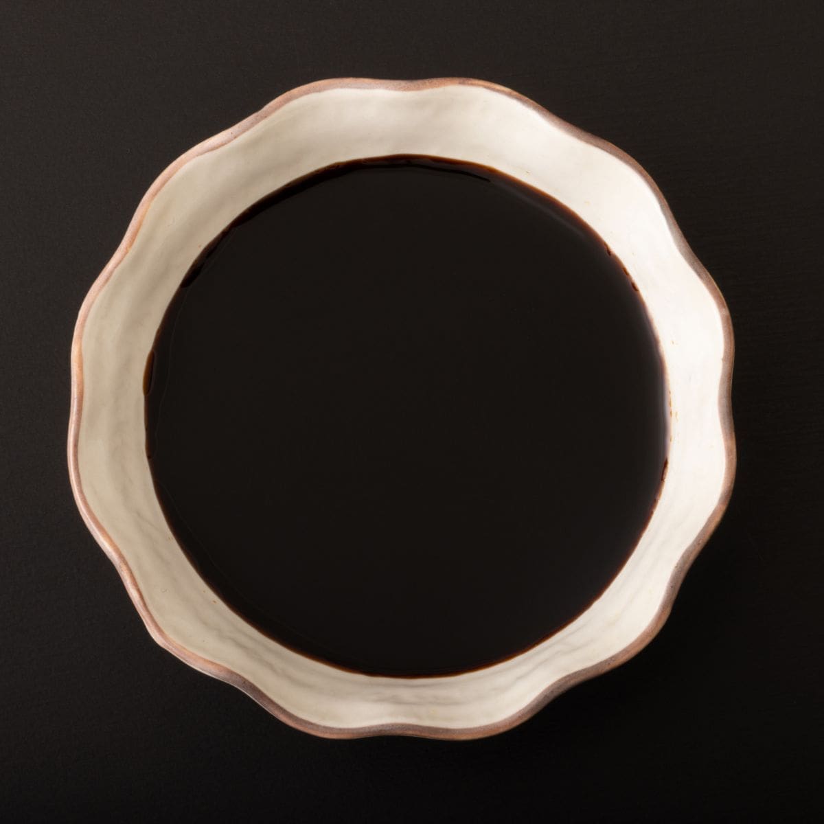 A close-up photo of a bowl of tamari on a black background.