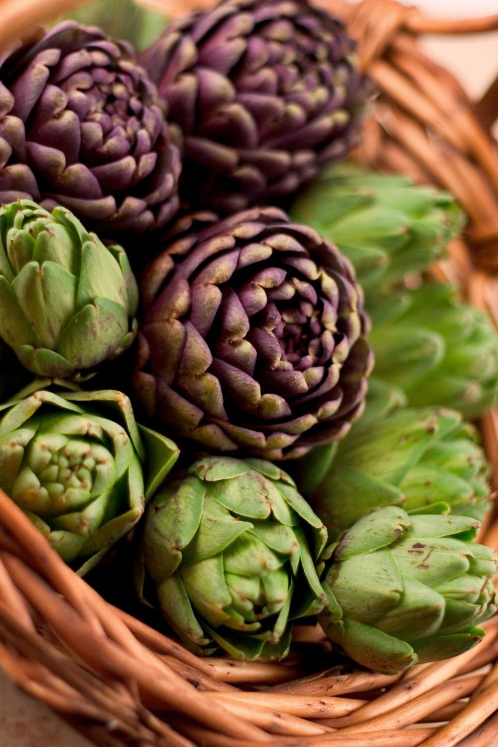 A wicker basket filled with green and purple artichokes. 