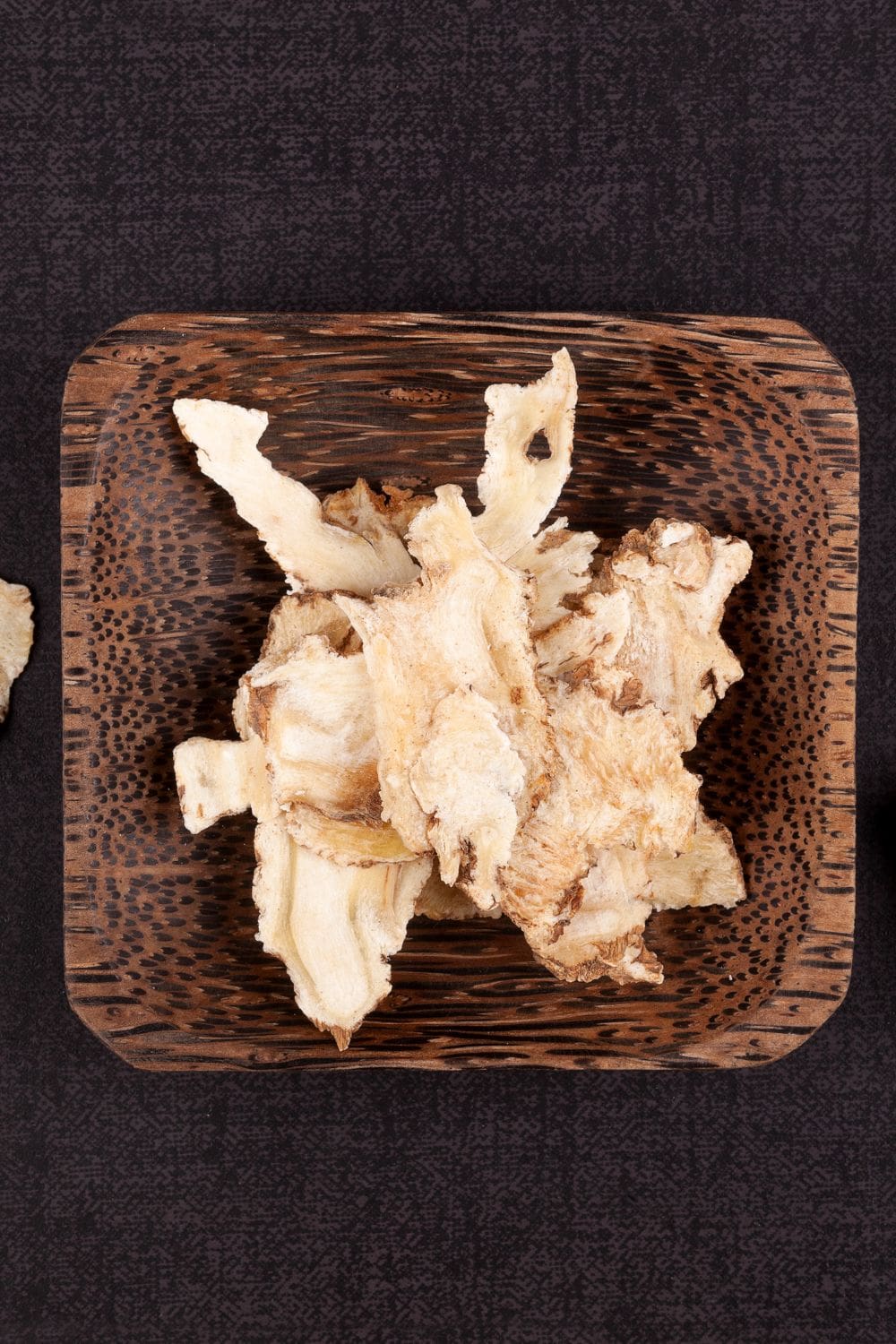 A rustic wooden bowl cradles a generous portion of freshly sliced angelica roots.