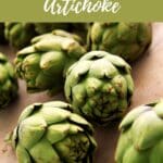 A rustic wooden table with a group of artichokes piled on top.