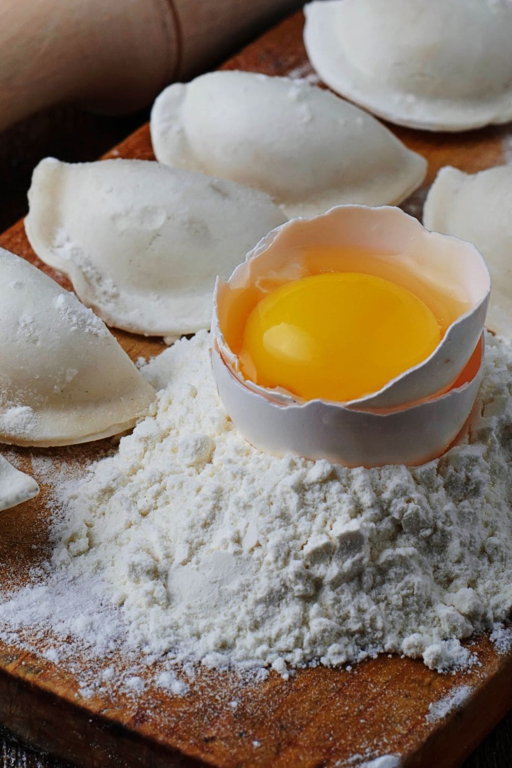 A close-up photo of a broken egg on top of a pile of flour on a wooden cutting board.
