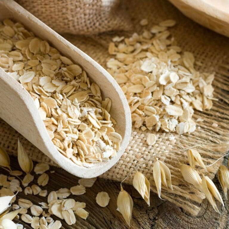 A wooden scoop filled with rolled oats sits on a rustic wooden table.