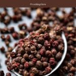 A close-up photo of a metal spoon filled with Szechuan peppercorns.
