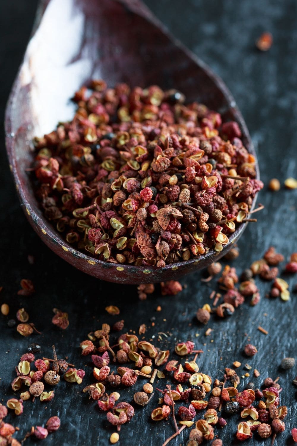 A close-up photo of a wooden spoon filled with Sichuan peppercorns
