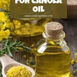 A clear glass bottle of canola oil is standing on a wooden table.