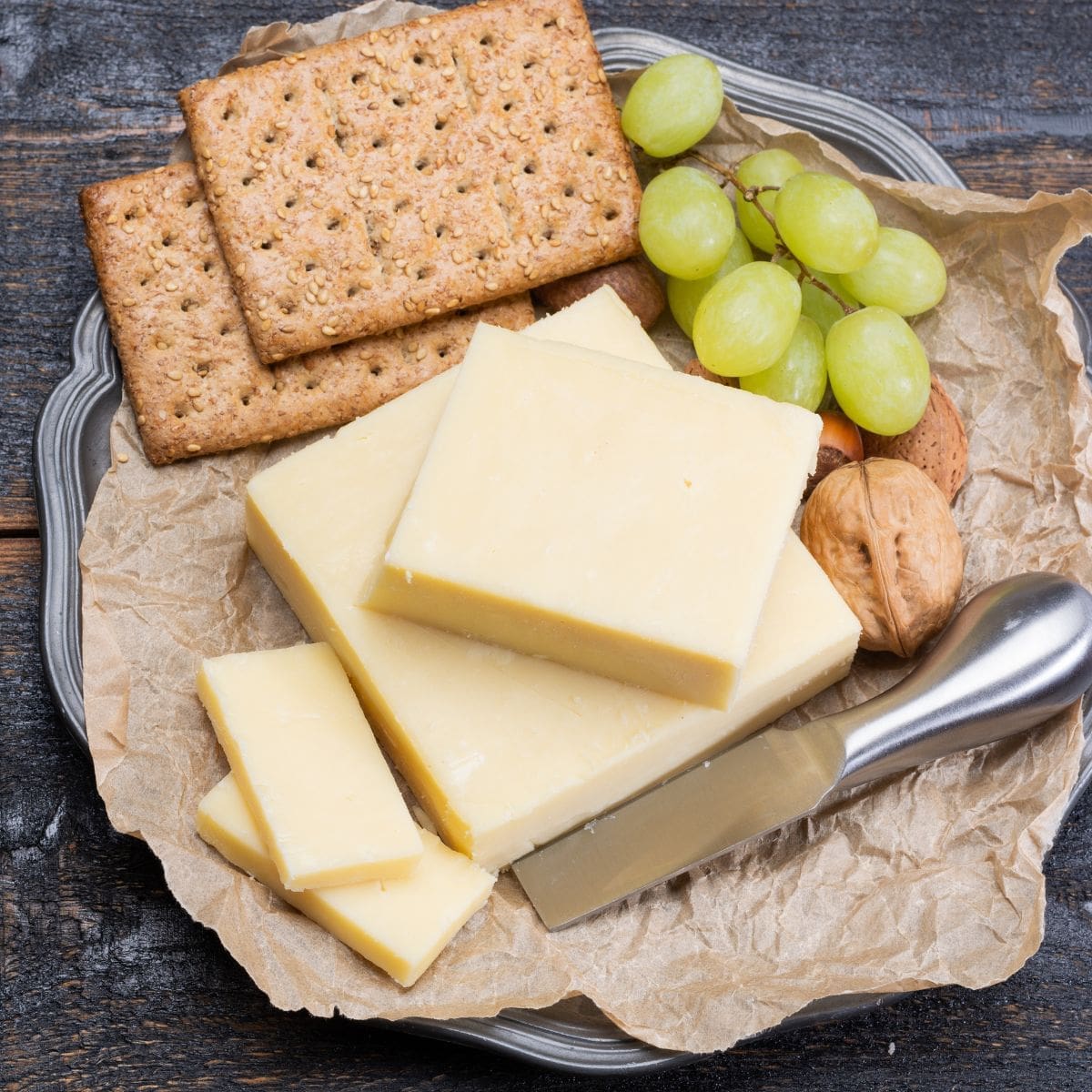 A close-up of a plate of white cheddar cheese, crackers, grapes, and nuts.