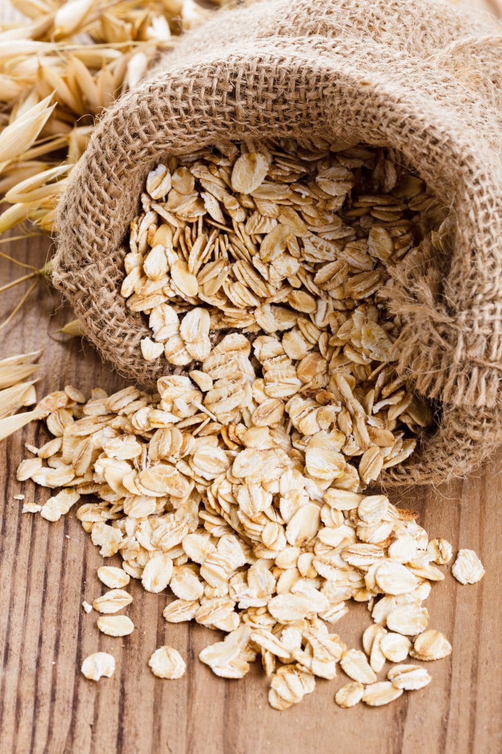 A burlap sack filled with rolled oats sits on a light wooden table.