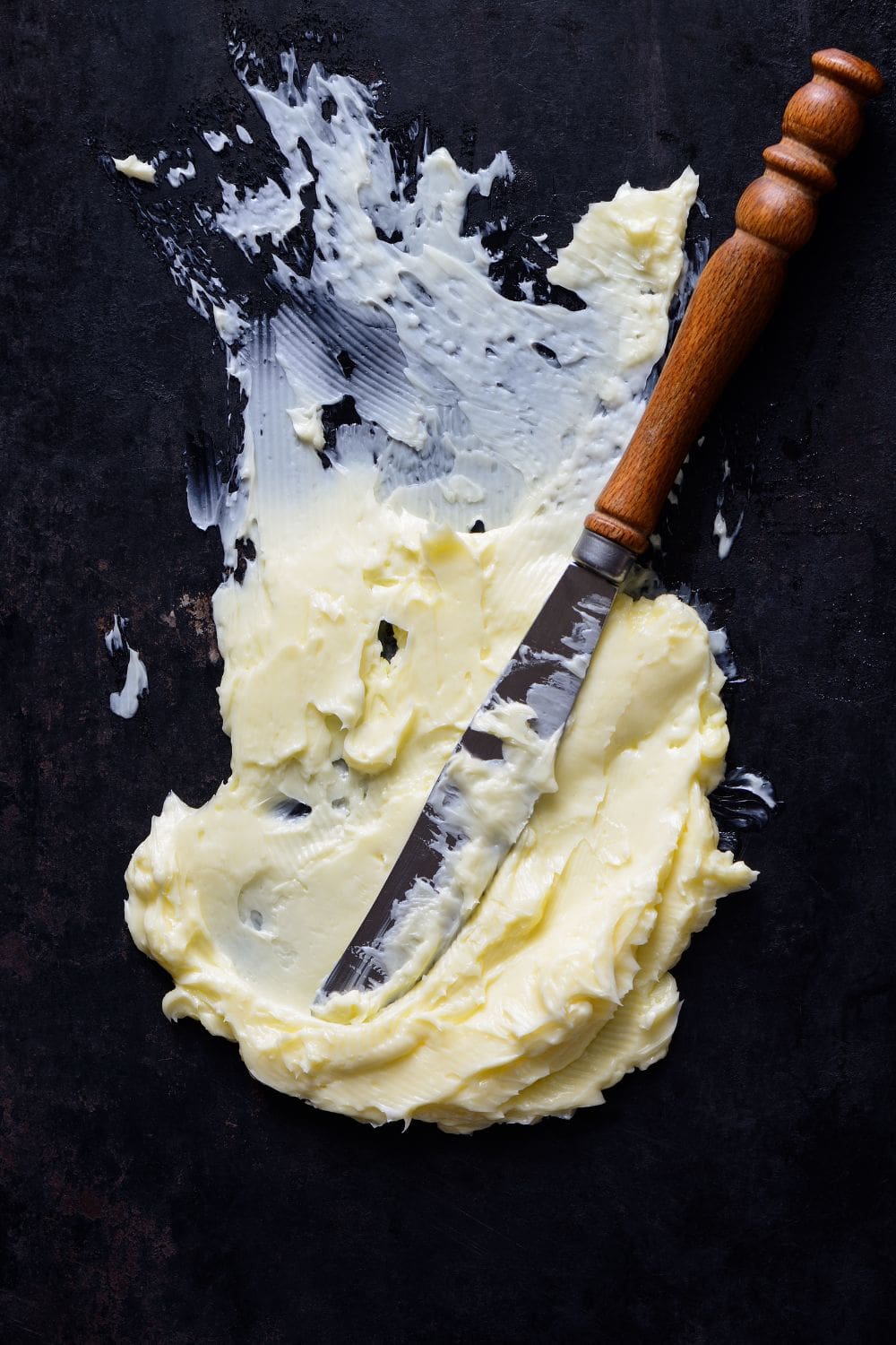A knife lying on top of a pile of margarine on a black surface.