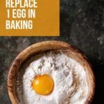 A wooden bowl filled with flour and an egg sitting on top of it.