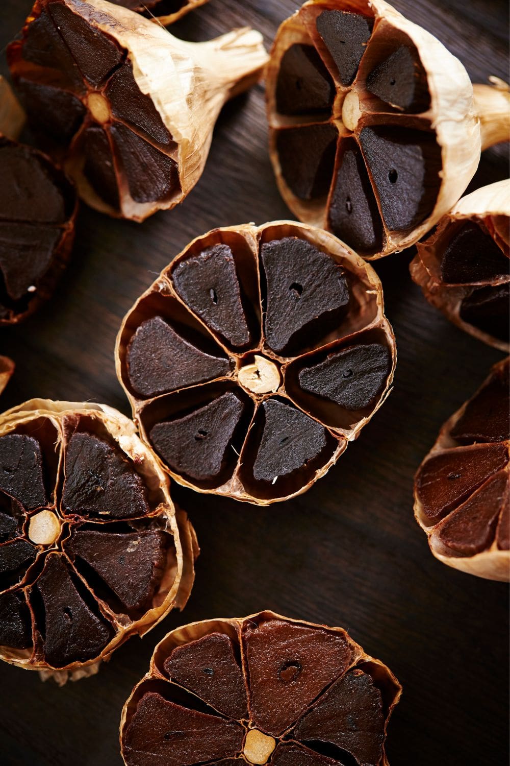 A close-up photo of several cloves of black garlic on a wooden cutting board.