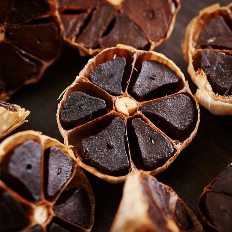 A close-up photo of several cloves of black garlic on a wooden cutting board.