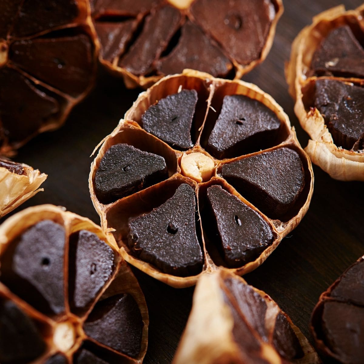 A close-up photo of several cloves of black garlic on a wooden cutting board.