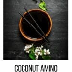 Coconut aminos with a blossoming cherry branch. On a black wooden background.