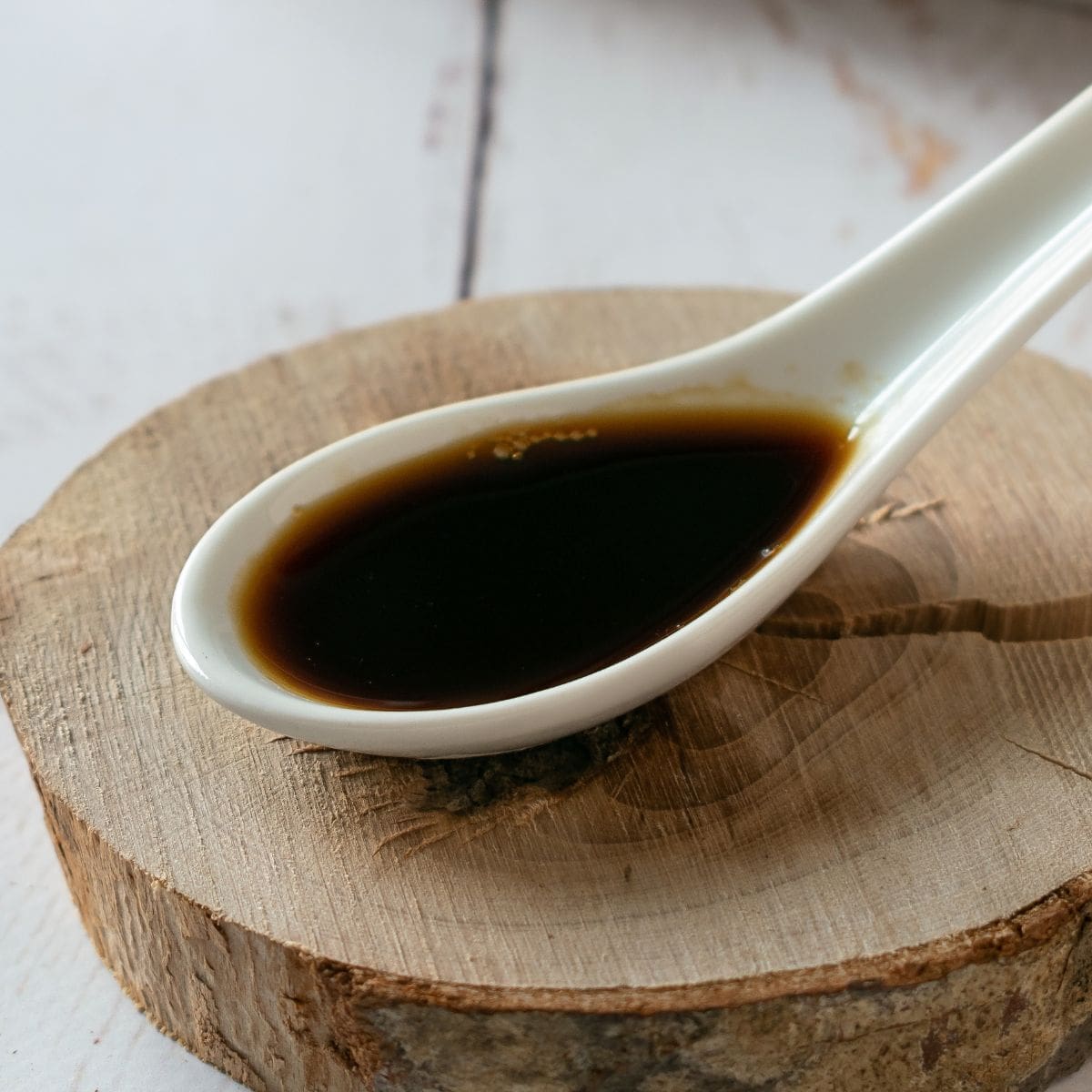 Coconut Aminos in a small white spoon on a wooden table.