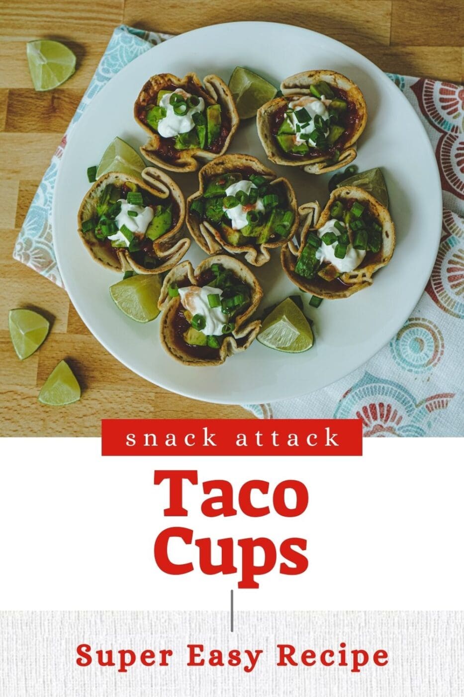 Taco cups topped with sour cream and green onions on a white plate. Lime slices are spread around. 