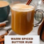 A close-up photo of a warm spiced butter rum cocktail in a clear glass mug.