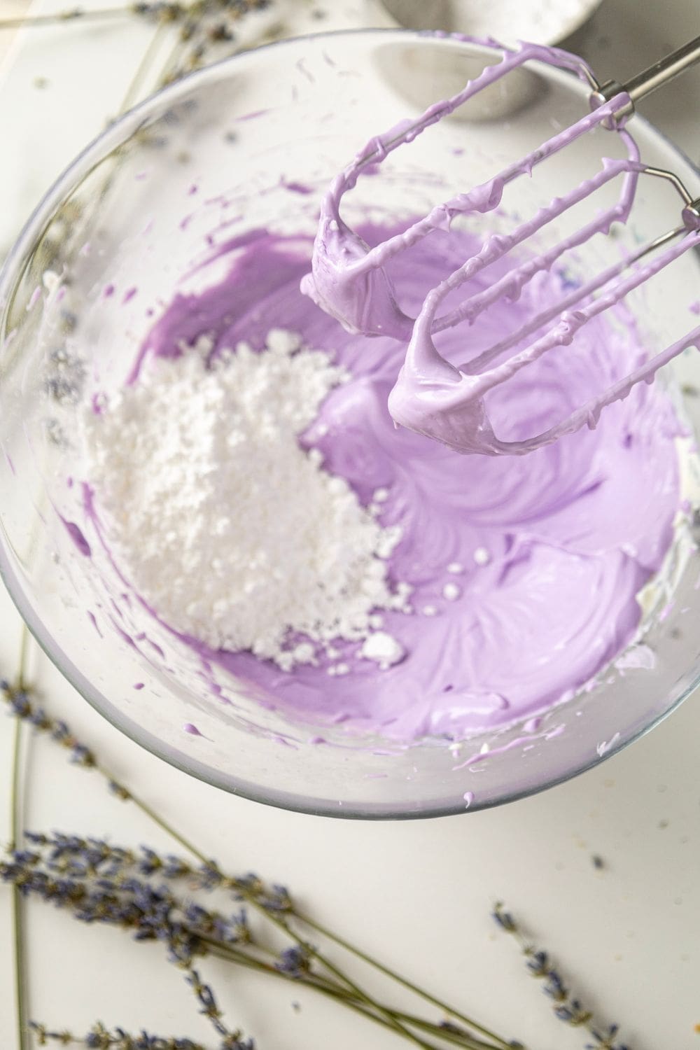 A glass bowl filled with purple frosting. Powdered sugar is dusted around the rim of the bowl.
