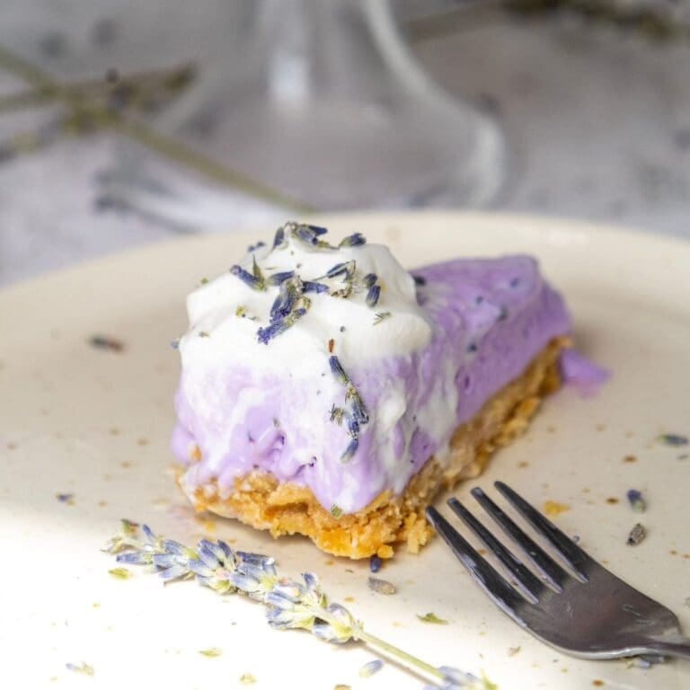 A slice of lavender cheesecake on a white plate with a fork.