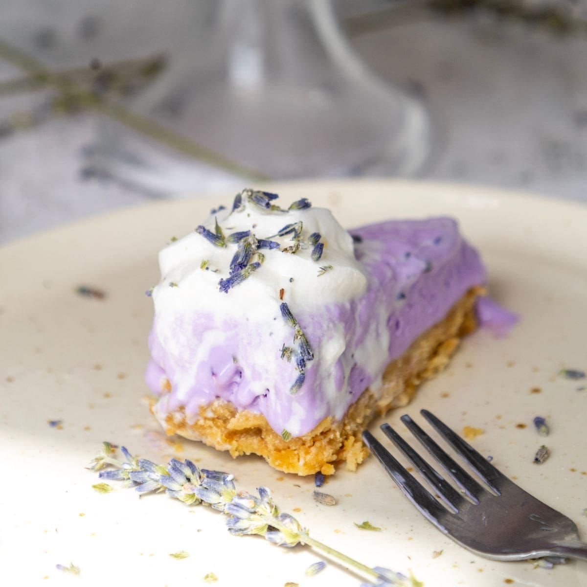 A slice of lavender cheesecake on a white plate with a fork.