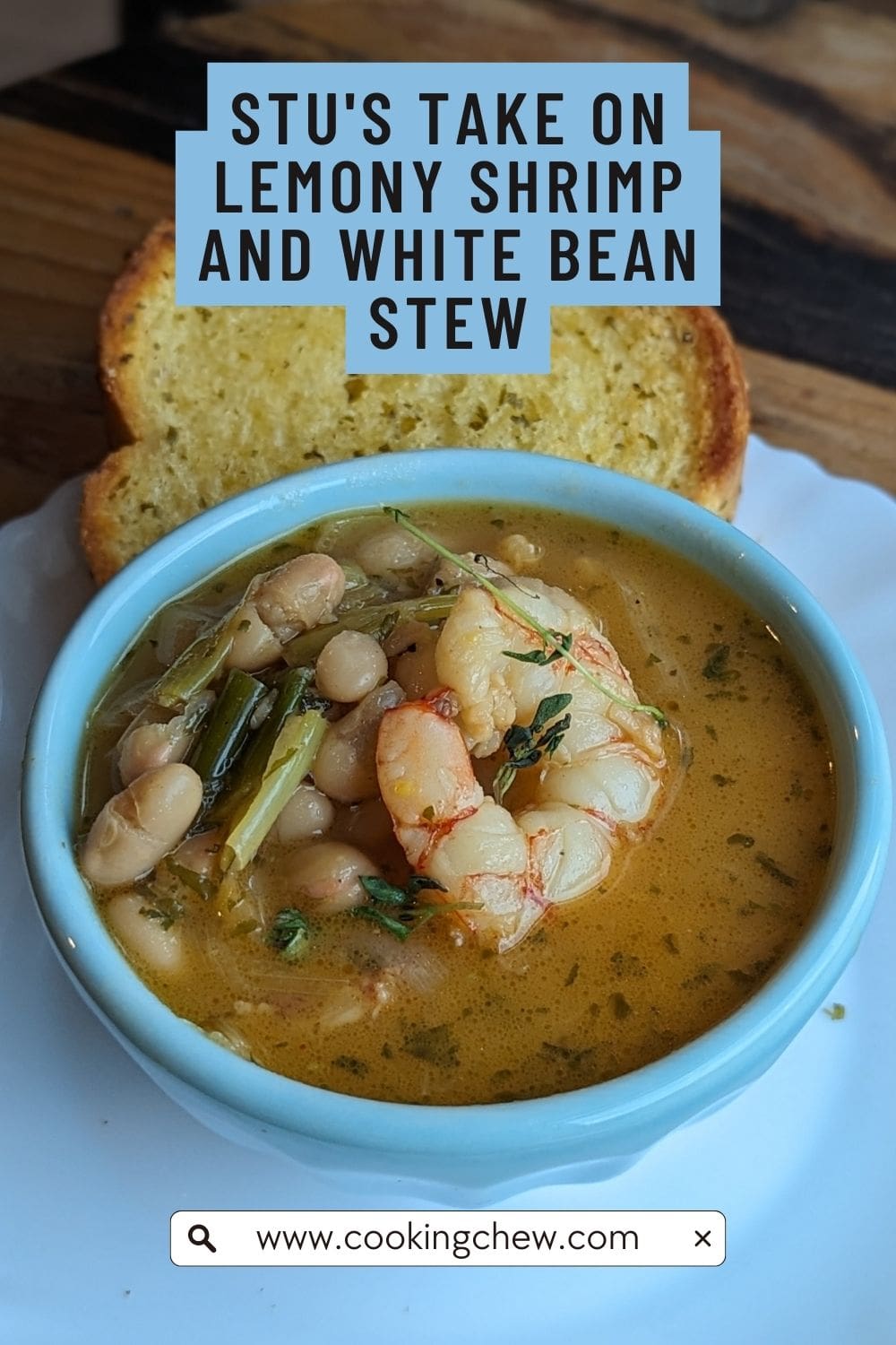 A white bowl filled with lemony shrimp and white bean stew with a slice of garlic bread sits next to the bowl on the plate.