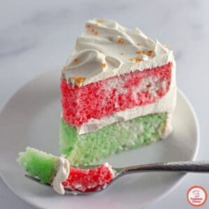 A slice of vibrant holiday Jello cake served with whipped cream topping.