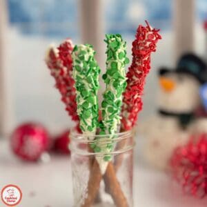Chocolate-dipped pretzel rods displayed on a holiday-themed table.