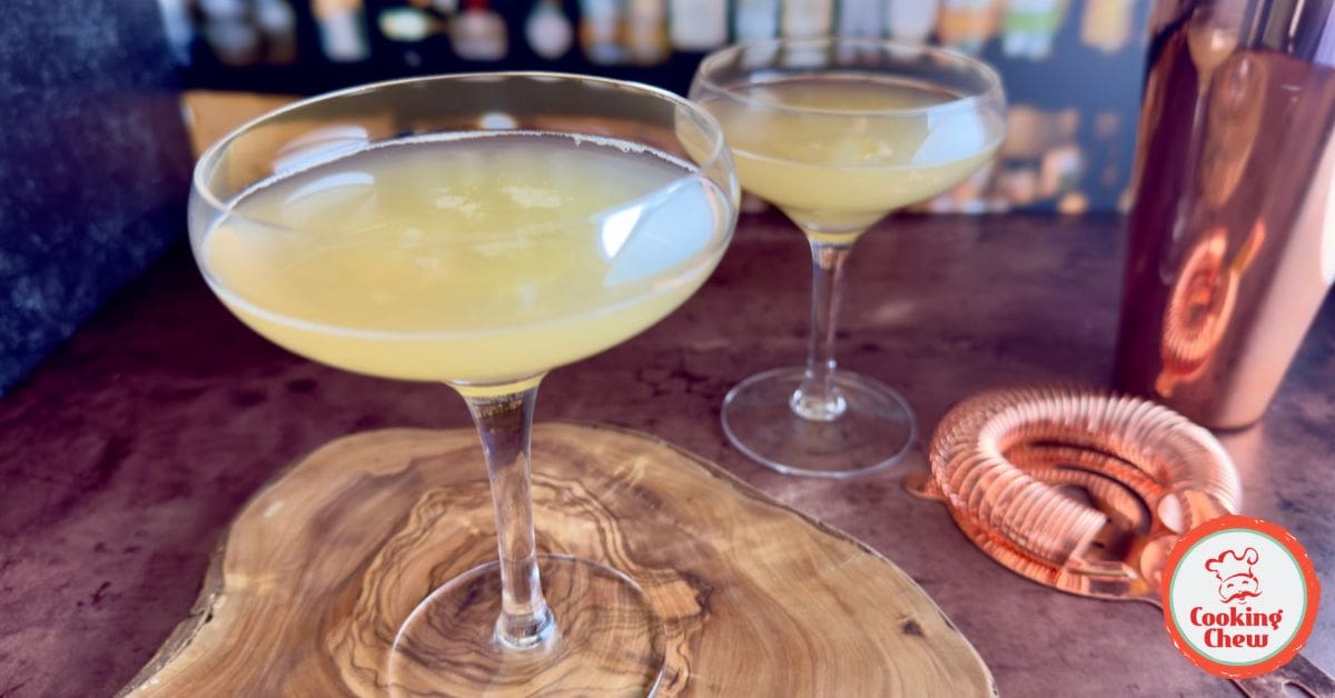 A glass of classic Whiskey Sour with a lime wedge and ice, served on a wooden bar.