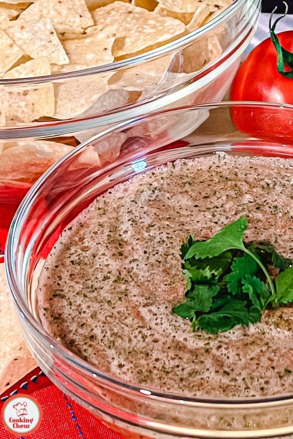 A bowl of fresh tomato salsa garnished with cilantro, served alongside crispy tortilla chips on a wooden table.