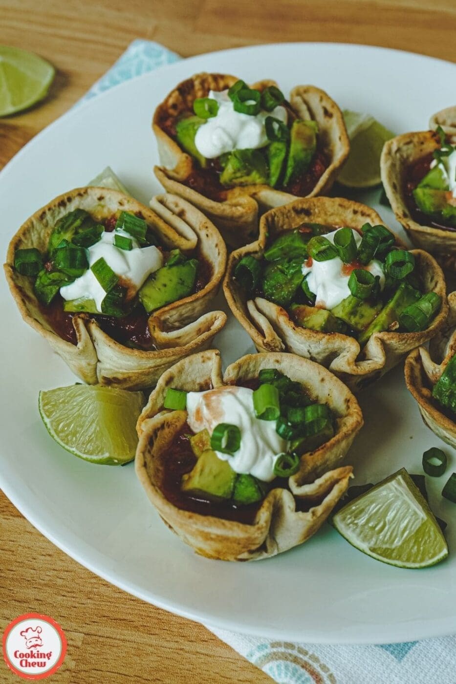 Bite-sized taco cups made with ground beef and tortillas, garnished with toppings and served on a platter.