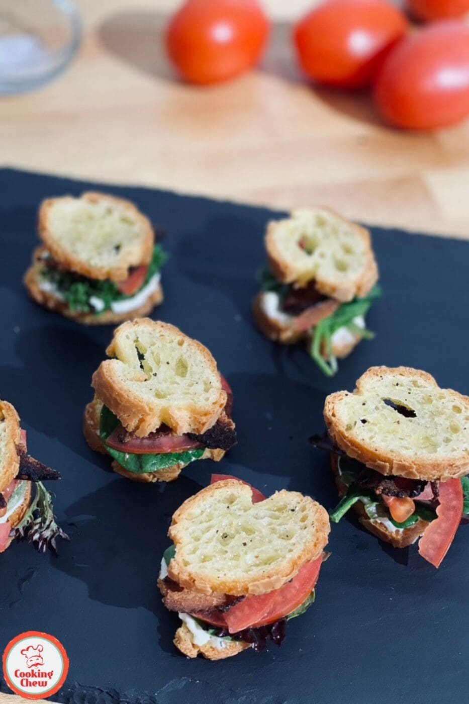A plate of mini BLT baguette sandwiches with crispy bacon, fresh lettuce, and tomatoes, served on golden baguette slices, perfect for party appetizers.