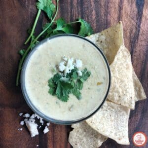 A festive bowl of queso dip with jalape&ntilde;o slices and colorful chips.