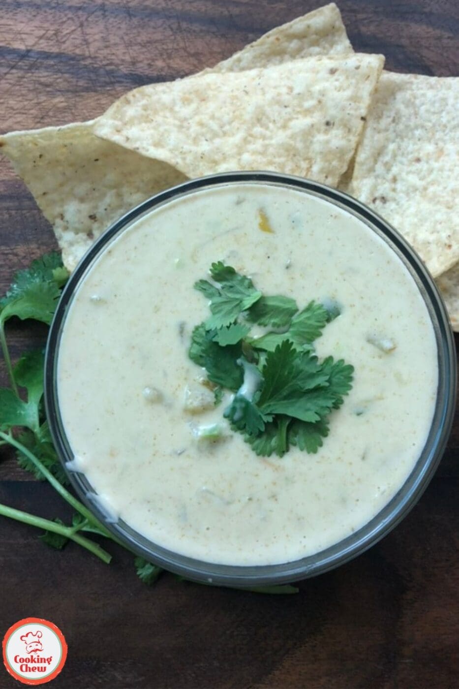 A slow cooker filled with creamy cheese dip garnished with diced tomatoes and green onions, served with tortilla chips on the side.