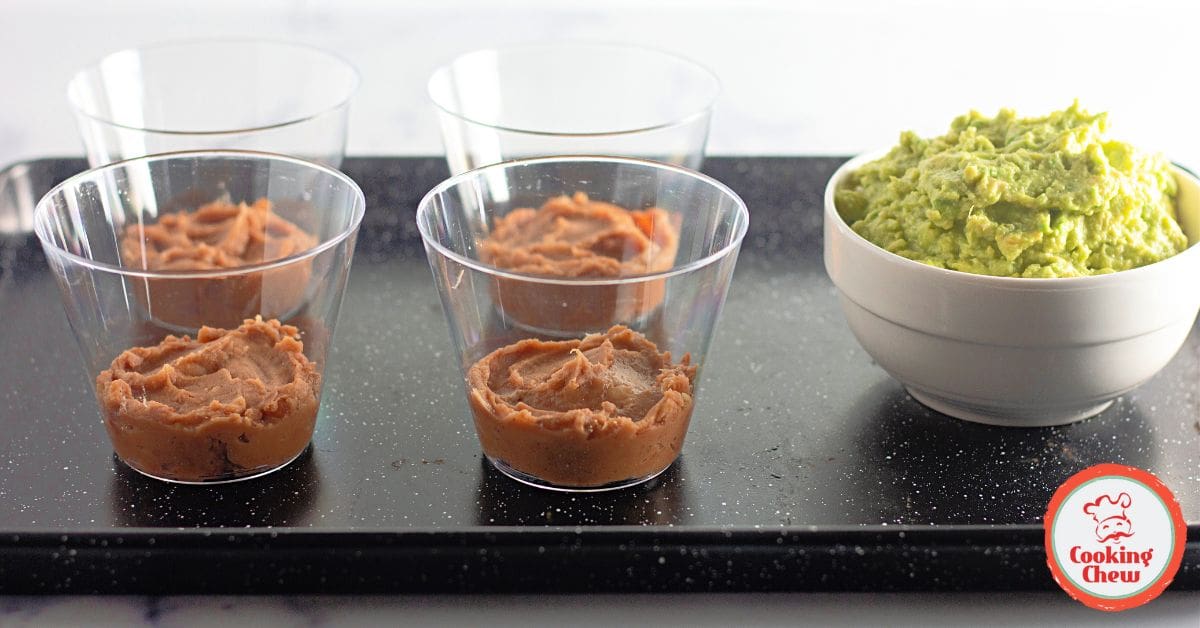 Tex-Mex dip cups arranged on a party platter with chips on the side.