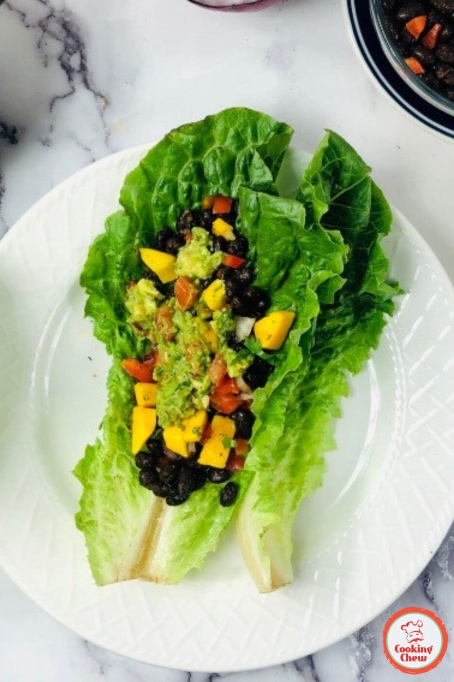 Fresh black bean lettuce wraps topped with homemade guacamole, served on a white plate.
