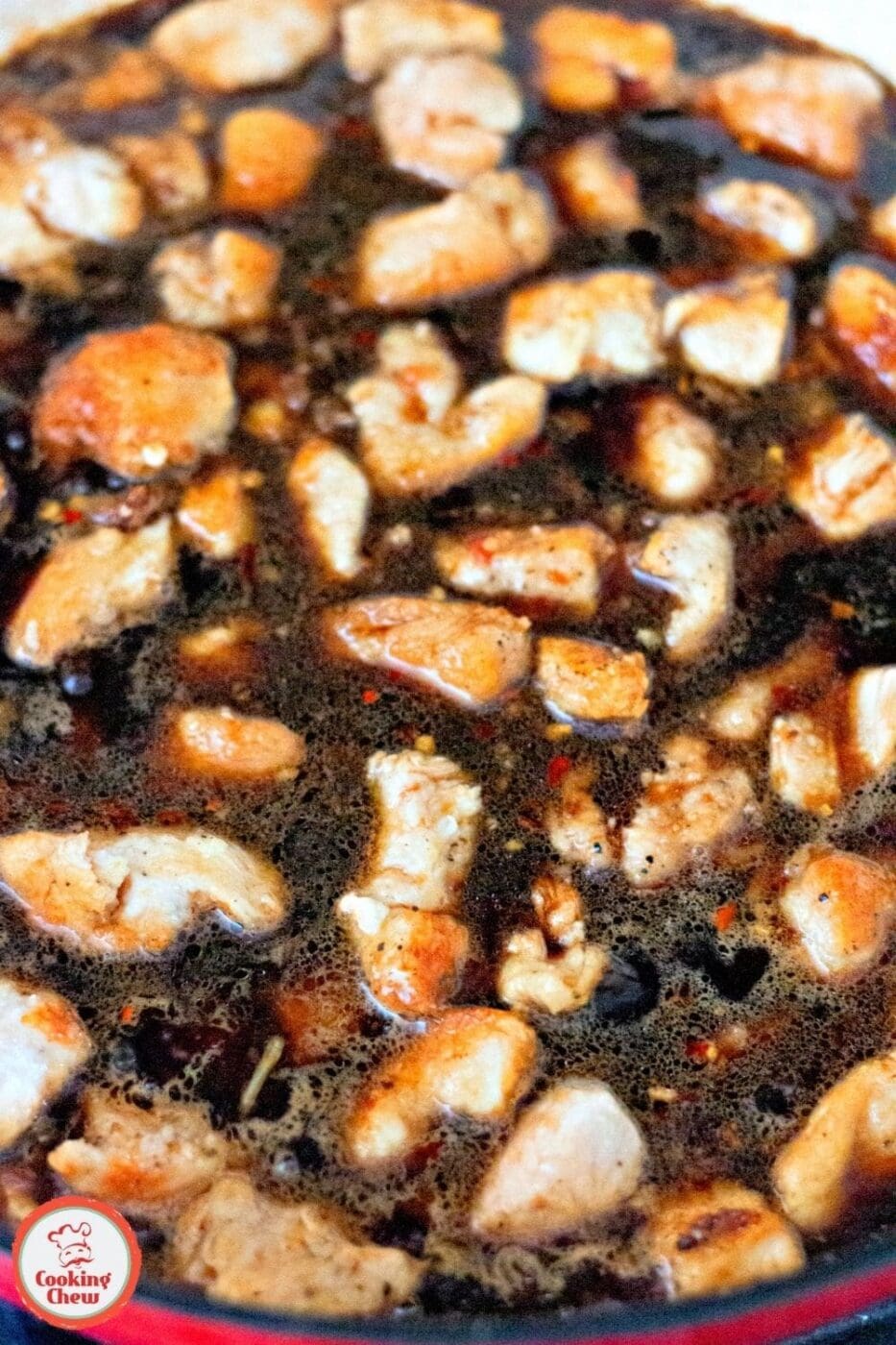 A cast iron skillet with sizzling bourbon chicken and a wooden spoon.