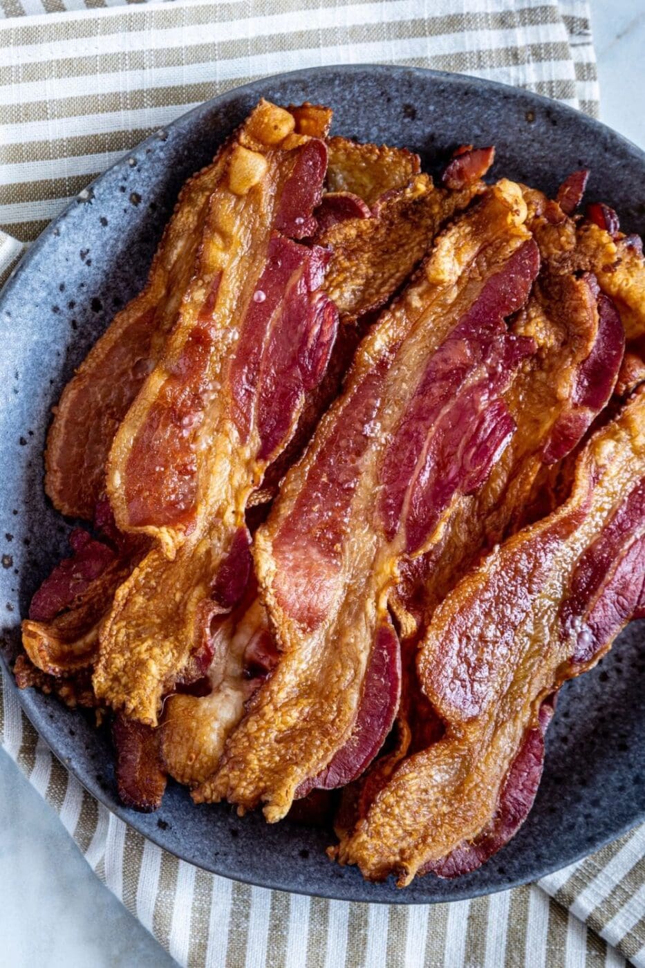 A baking sheet with crispy, golden-brown bacon slices fresh out of the oven, resting on parchment paper.