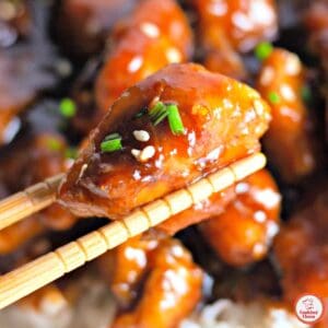 chopstick lifting a bite of glazed bourbon chicken.