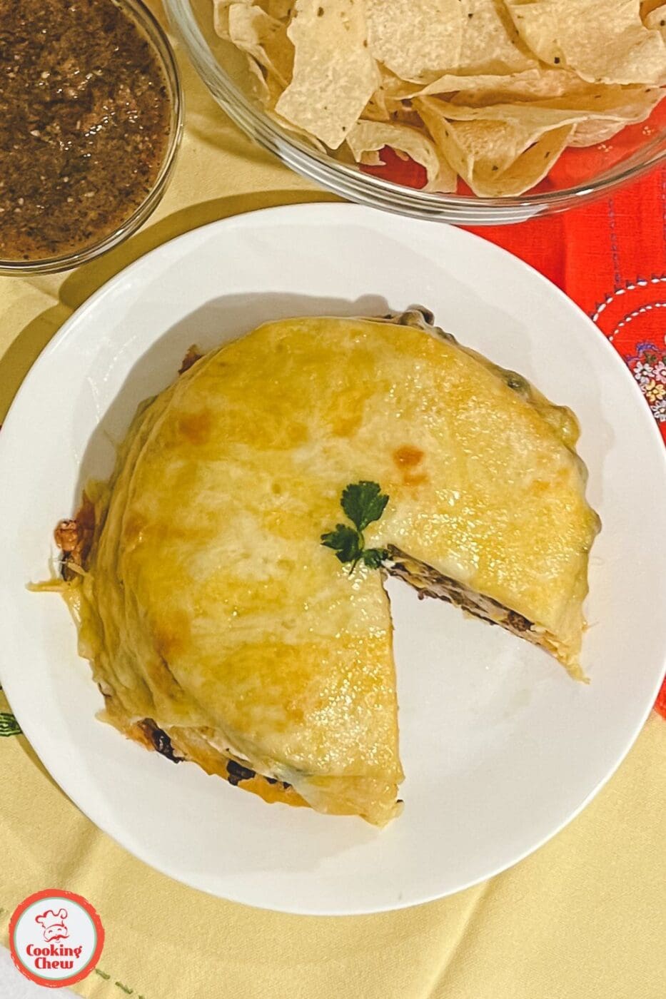 A layered Mexican tortilla casserole with melted cheese, seasoned beef, and fresh toppings on a plate.