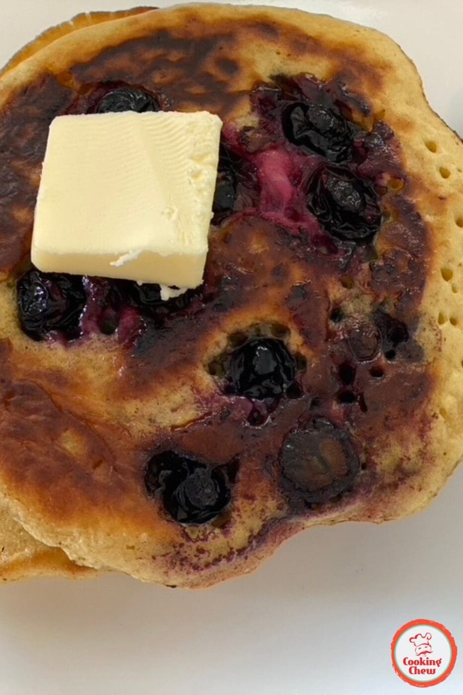 A stack of fluffy blueberry pancakes topped with fresh blueberries and drizzled with syrup.