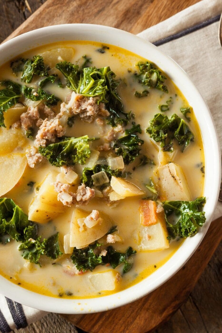 A steaming bowl of creamy sausage and potato soup garnished with fresh herbs.