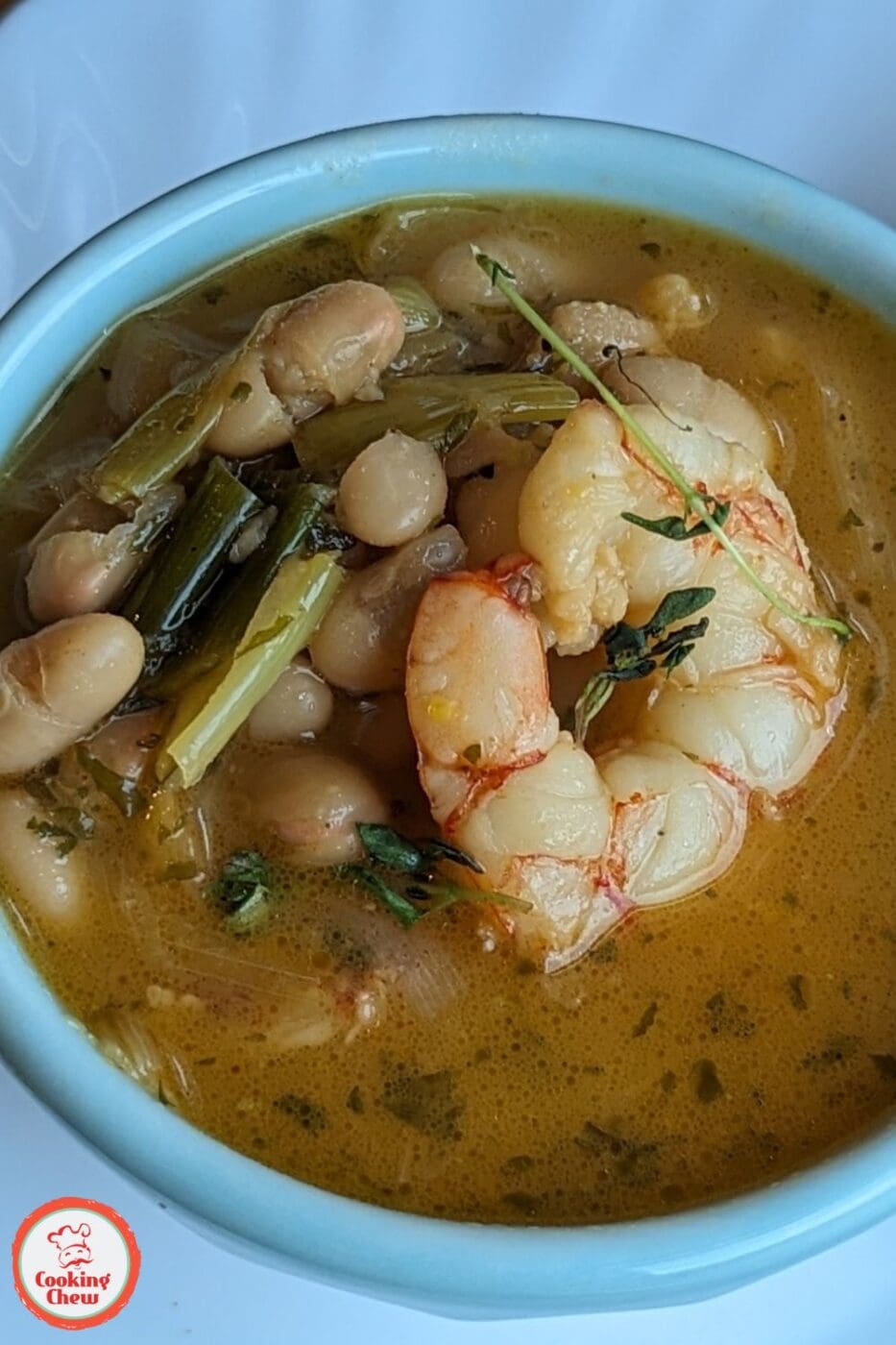 A bowl of shrimp and white bean stew in a lemony broth, garnished with fresh herbs.