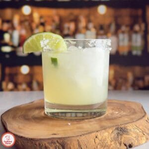 A bartender pouring a freshly mixed margarita into a glass over ice.