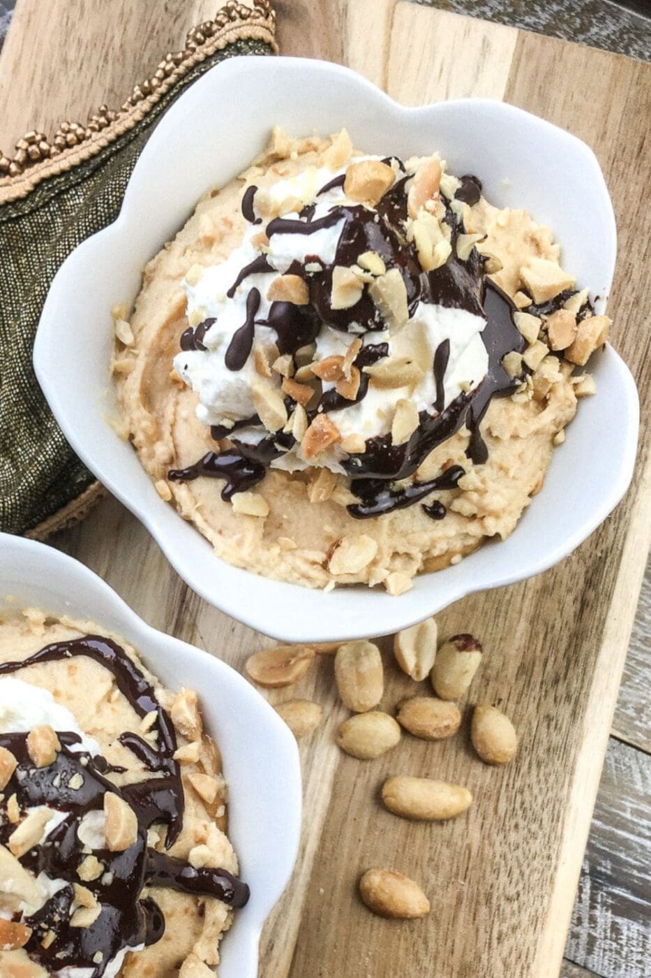 A glass of peanut butter mousse parfait topped with chocolate drizzle and crushed nuts.