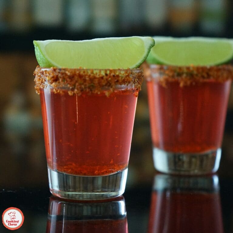 A bright red tequila shot with a spicy Tajín rim and a fresh lime wedge.