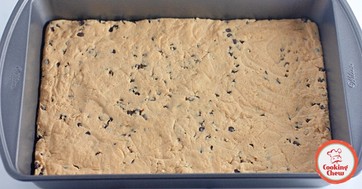 A hand holding a soft peanut butter cookie bar, showing its chewy texture.