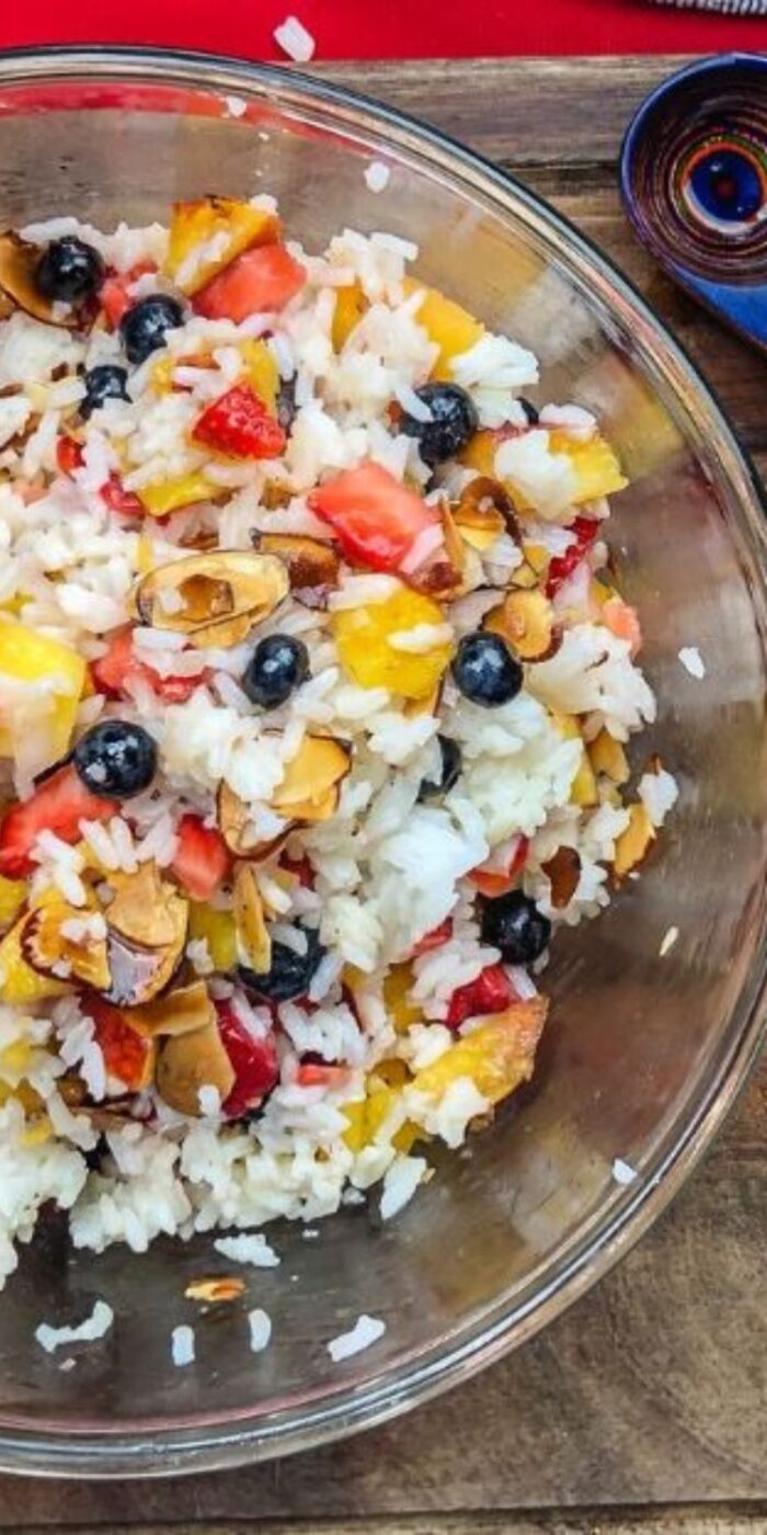 A white bowl of chilled rice salad with sliced peaches, berries, and almonds, perfect with lemon pepper chicken.